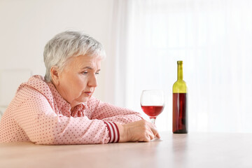 Stressed senior woman drinking wine at home