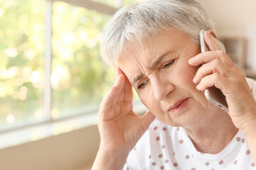 Stressed senior woman talking by mobile phone at home