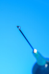 Syringe needle with liquid drop on the tip macro close up isolated on blue