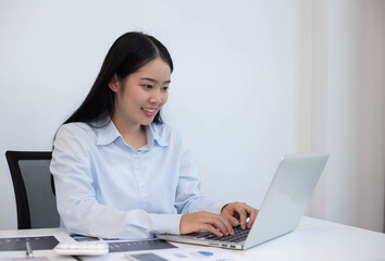 An Asian business woman sits at a desk with a laptop computer in a modern office.