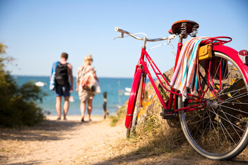 Couple allant à la plage laissant leur vieux vélo rouge sur le chemin.