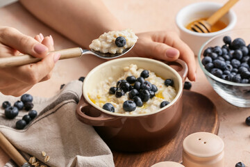 Woman eating tasty oatmeal with blueberry in bowl on table