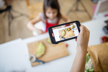 Female hand with a smartphone recording a little girl cutting an avocado