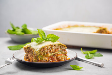 Homemade oven-baked green lasagna with spinach in the dough, ragu - meat sauce, bechamel and parmesan cheese. Fresh spinach salad  and casserole on background.