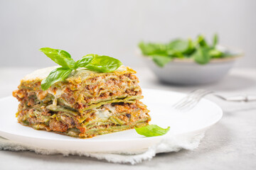 Portion of homemade oven-baked green lasagna with spinach in the dough, ragu - meat sauce, bechamel and parmesan cheese. Fresh spinach salad on background. Close-up.