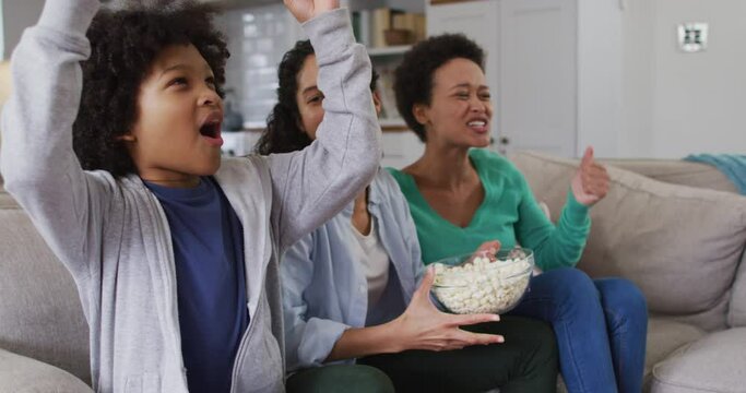 Mixed race lesbian couple and daughter watching tv eating popcorn high fiving