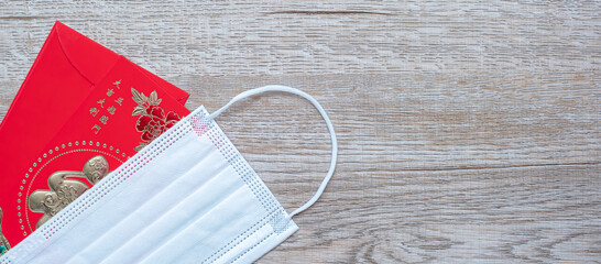 Fototapeta premium Red envelope or Ang pao and Medical face mask against Coronavirus disease infection. Chinese character means happiness or good fortune, and Chinese sentence means Lucky and Wealthy. Lunar New Year