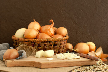 A lot of onions in a wicker basket on a brown background. Onions whole and chopped on a cutting board. Vegetables in the cooking process. Onions on a textured background.