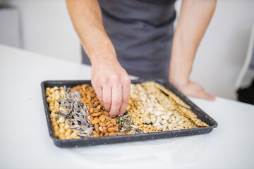 Male hand picking seeds from a black tray with seeds and nuts