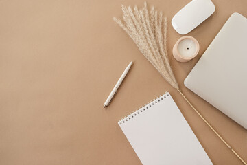 Flatlay of spiral flip notebook with blank paper sheet. Laptop, pampas grass, stationery on beige...