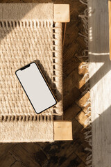 Blank screen smart phone on rattan chair. Flat lay, top view. Copy space mockup template. Warm...