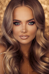 Fototapeta premium Beautiful blond woman with long lashes and wavy hair posing on golden background