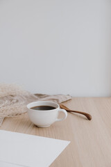 Blank paper sheet on beige wooden table. Artist home office desk workspace with washed linen blanket, coffee cup, pampas grass. Wedding invitation card. Mockup with empty copy space.