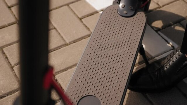 Close-up of a businessman in black leather shoes walks up to the electric scooter and removes the stand with his foot.