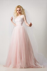 beautiful blonde girl in a pink wedding dress posing in the studio on a light background