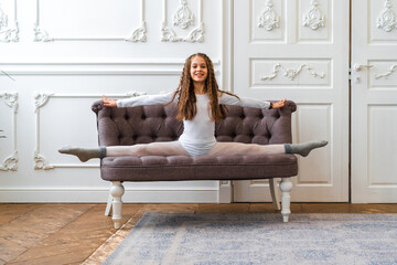 Little girl doing rhythmic gymnastics in white interior with sofa