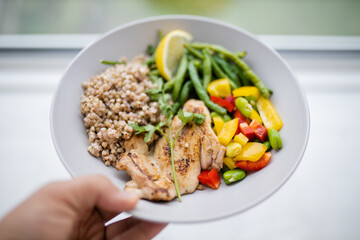 Hand holding a chicken and buckwheat dish with green beans