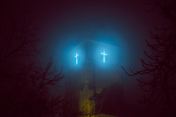 leuchtendes Kreuz am Kirchturm nachts im Nebel