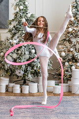 A beautiful little gymnast in a white sports dress doing rhythmic gymnastics exercises spirals with...