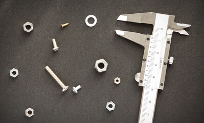 A CALIPER, SCREWS AND NUTS ON A BLACK SURFACE.