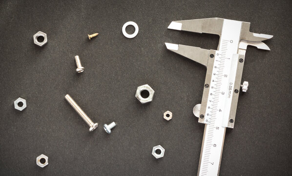 A CALIPER, SCREWS AND NUTS ON A BLACK SURFACE.