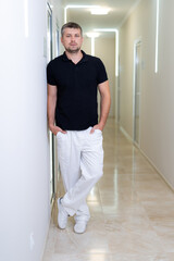 Male handsome dentist posing to the camera in modern clinic corridor. Light hospital interior.