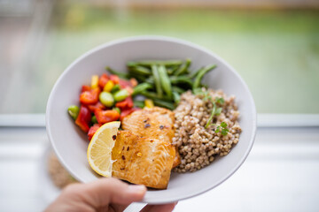 Hand holding salmon and buckwheat dish with green beans