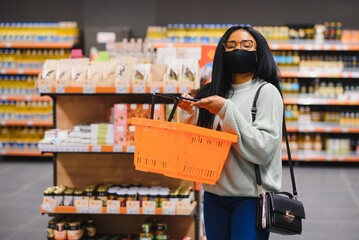 African woman wearing disposable medical mask. Shopping in supermarket during coronavirus pandemia outbreak. Epidemic time.
