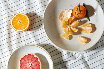 food, healthy eating and fruits concept - close up of mandarin, grapefruit and orange on plates over drapery