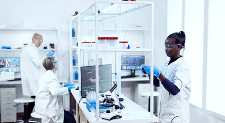 Multiethnic scientists team working together in modern facility doing virus analysis. Black healthcare researcher in biochemistry laboratory wearing sterile equipment.