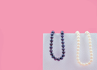 Few beads of pearls hanging on a white box on pink background, with copy space.