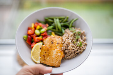 Hand holding salmon and buckwheat dish with green beans