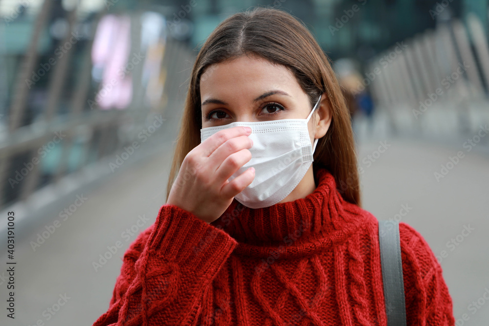 Wall mural Close up of young woman adjusting protective mask on nose looks at camera outdoors