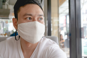 Fototapeta na wymiar Asian man wears white mask for Covid virus protection in public cafe.