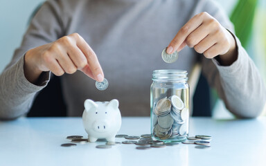 Closeup image of a woman putting coin into piggy bank and a glass jar for saving money concept