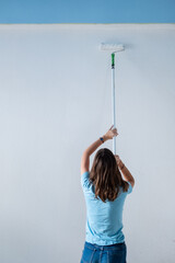 Renovierung einer Wohnung - Eine Teenagerin streicht mit einer Farbrolle eine weiße Wand mit...