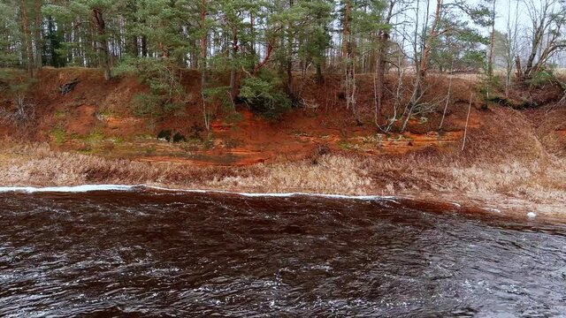 Red sandstone cliffs in the banks of river Salaca during late autumn time, Latvia. Real time drone footage