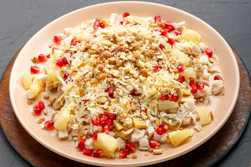 A plate with salad with chicken, pineapple, pomegranate and nuts on a concrete background on a wooden stand close-up.