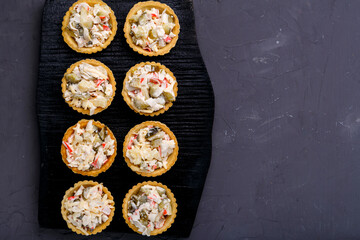 Tartlets with pineapple and shrimp salad on a black wooden board on a gray concrete background copy space