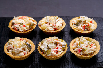 Tartlets with salad on a black wooden board on a gray concrete background.
