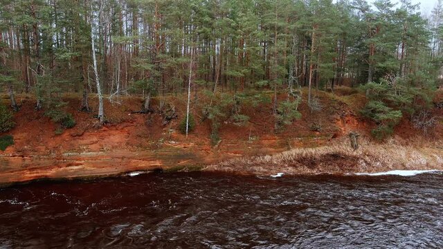 Red sandstone cliffs in the banks of river Salaca during late autumn time, Latvia. Real time drone footage