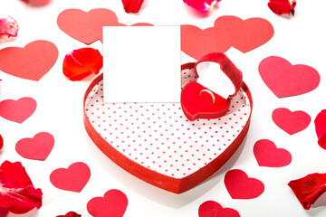 Ring in a box in the shape of a heart on a white background with a note in the middle of rose petals and red hearts.