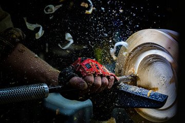 Gloved hand operates a wood lathe with wood shavings flying away.