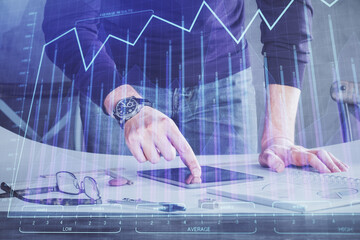 Double exposure of man's hands holding and using a digital device and forex graph drawing. Financial market concept.