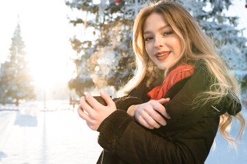 A beautiful girl with long wavy hair in a black jacket in whose hands a mug stands in a snowy park