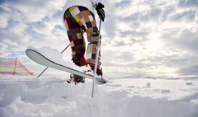 Close-up, low angle view snapshot of skier's legs. Man skiing, making a jump up on white snowy surface against beautiful cloudy sky. Copy space. Concept of winter sport activities.