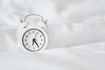 white alarm clock on messy white bed sheet , early wake up , awaken  or reminder concept with copy...
