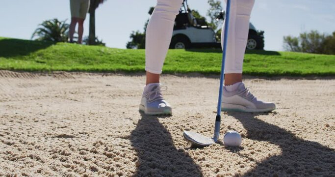 Two caucasian women playing golf one taking shot from bunker