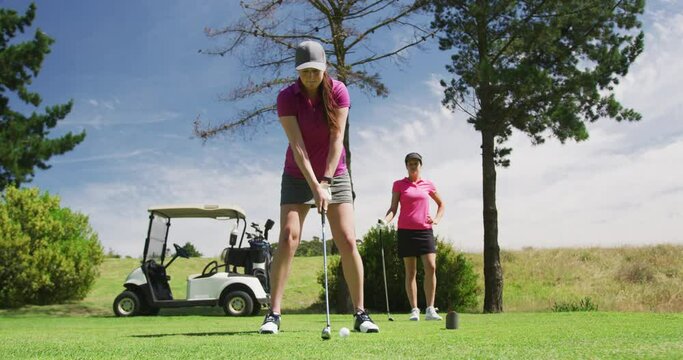 Two caucasian women playing golf one taking shot from bunker