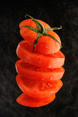 Ripe red tomato cut into slices and tossed into the air isolated on black background.